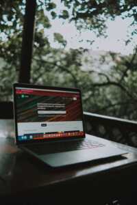 Open laptop showing a website screen on a wooden table in an outdoor terrace setting.