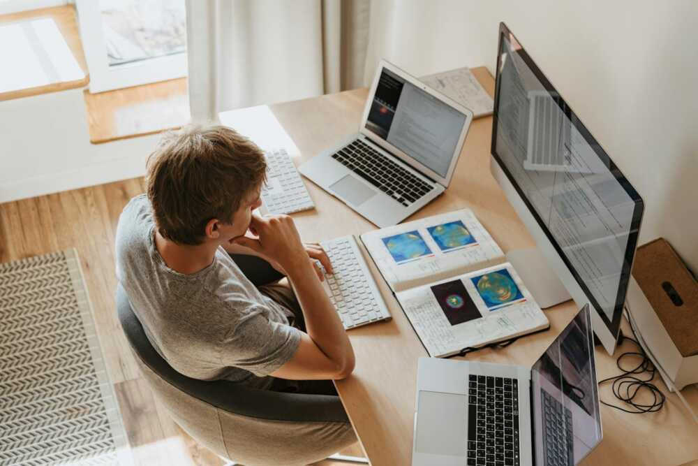 Top view of young programmer working on multiple laptops in a modern office setting.