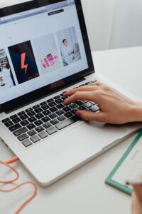 Close-up of hand with manicured nails browsing online store on laptop.